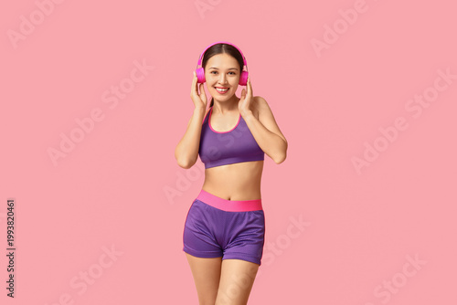 Photography Young woman in sportswear listening to music on pink background