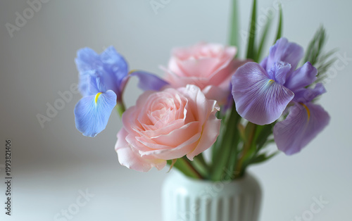 Delicate pink roses and blue irises arranged in a simple white vase with soft lighting