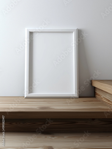 Blank white picture frame leaning against a white wall on a wooden surface