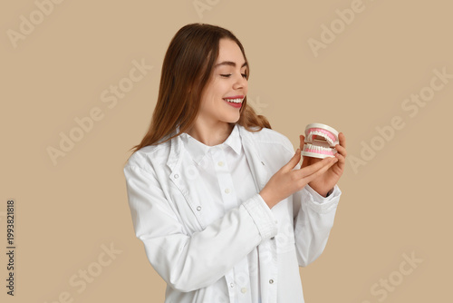 Female dentist with jaw model on beige background. World Dentist Day