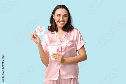 Fotografía Beautiful young woman holding menstrual pads and paper with drawn flower on blue background