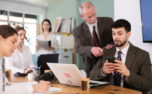 Photography Senior male boss chastises male subordinate for idleness and scrolling of phone, social networks and stealing personal and working time