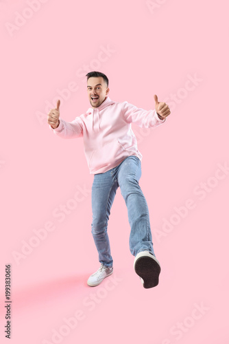 Happy young man showing thumbs-up on pink background