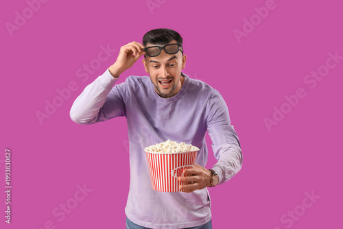 Happy young man with 3D glasses and popcorn on purple background