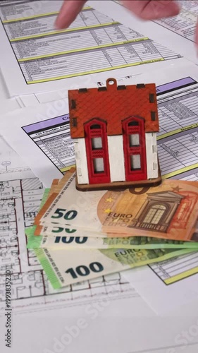 Close-up of a real estate agent placing euro banknotes and a house model on architectural blueprints, symbolizing property sale, investment deal, and real estate transaction process. 