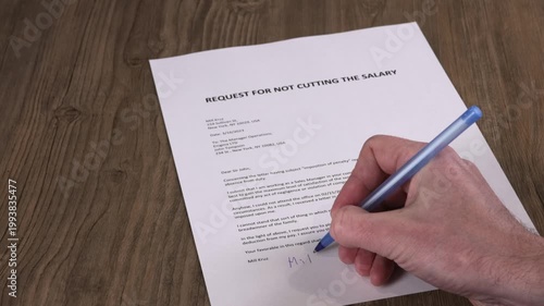 Close-up of a male hand signing a request for not cutting the salary. Workplace negotiation, employee rights, HR paperwork and corporate decision concept. 