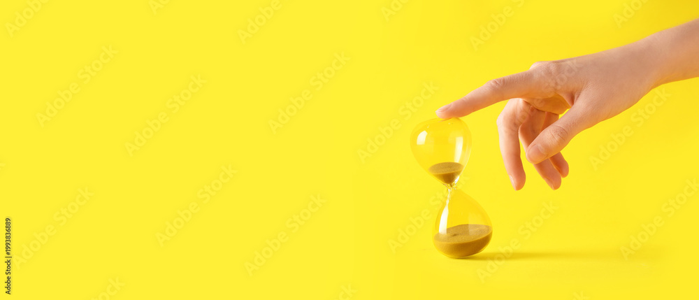 Fototapeta premium Female hand with stylish hourglass on yellow background