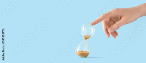 Tableau sur toile Female hand with yellow sand in stylish crystal hourglass on blue background