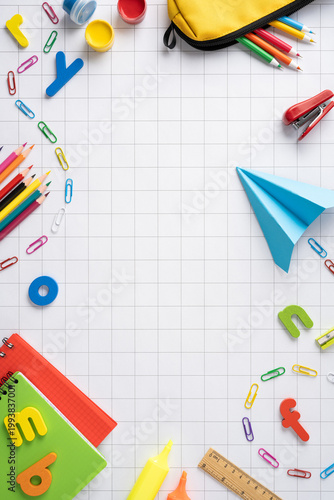 Back to school vertical flat lay with colorful supplies, pencils, paper plane and notebook on graph paper