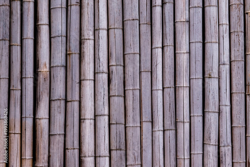 Billede på lærred Bamboo sticks arranged vertically create a textured pattern on a wall in natural
