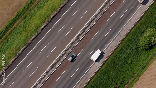 Highway aerial view: An aerial perspective captures the flow of traffic on a multi-lane highway, with cars and a truck navigating the asphalt under a clear sky, bordered by green fields and trees.