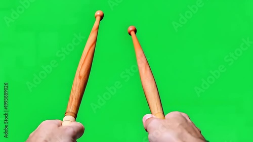 Hands holding wooden drumsticks on green screen background, ready for rhythmic music performance