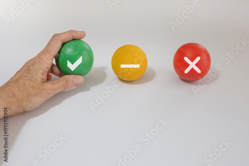 A hand reaches out to pick up a green ball marked with an OK symbol, placed next to a yellow ball with a neutral symbol and a red ball with a cross.