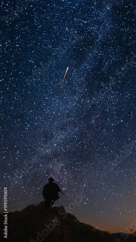 Man on a mountain top watching the night sky and celebrating shooting stars. Vertical design in 9:16 ratio. Smartphone and social media ready.