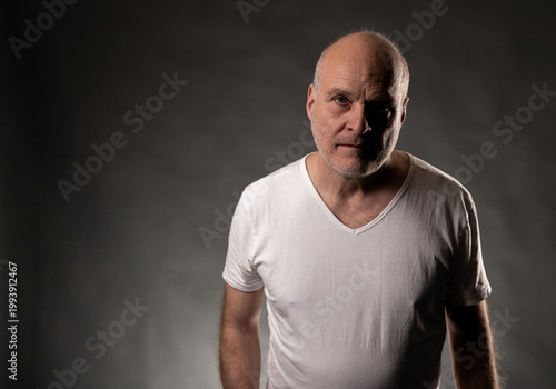Obraz na plátne Bald mature man posing with serious expression in low key studio lighting