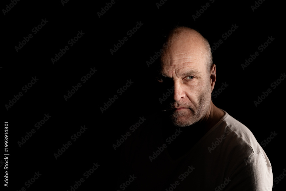 Obraz premium Serious bald man in low key lighting with mysterious shadows on his face