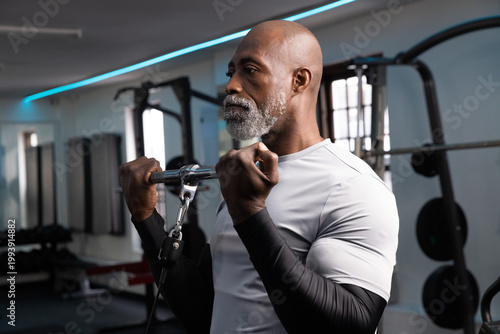 Obraz na plátně African American senior man performing cable biceps curl in gym in gray top hold