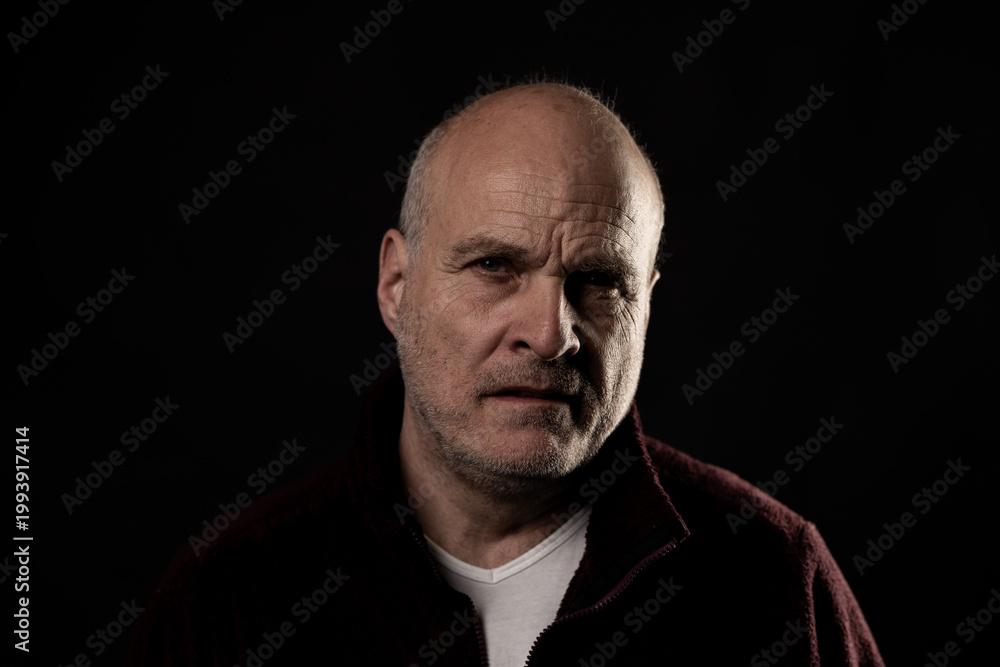 Obraz premium Older man expressing deep thought and seriousness on a black background, facing the viewer