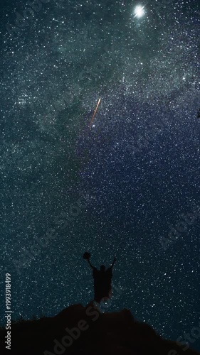 Man on a mountain top watching the night sky and celebrating shooting stars. Vertical design in 9:16 ratio. Smartphone and social media ready.
