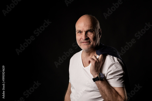 Obraz na plátně Senior man smiling wearing white t shirt and watch holding jacket over shoulder