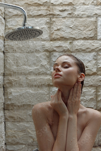 woman showering under rainfall showerhead in modern bathroom with textured stone wall, natural skin care, relaxation, calm expression, wet hair
