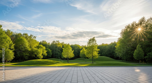 Vibrant green park landscape with rolling hills and lush trees under a bright blue sky illuminated by golden sun rays and a paved foreground