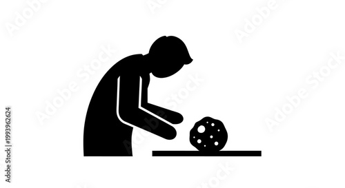 A person in a black silhouette is intently examining a spherical object with holes on a flat surface