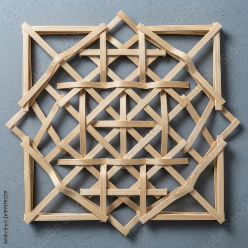 A handcrafted square lattice pattern made from light wooden sticks forms an intricate geometric design against a textured grey background.