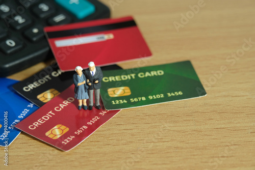 Miniature people toys conceptual photography. Elderly couple standing above credit card, paying, and buying household stuff
