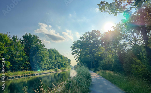 Принти на полотні A serene pathway lines a tranquil canal, embraced by lush greenery and gentle su