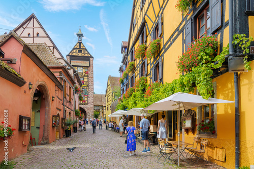 Φωτογραφία The Dolder Belfry Clock Tower can be seen from a cobblestone street of shops and cafes in the medieval old town of Riquewihr, France, in the Alsace region
