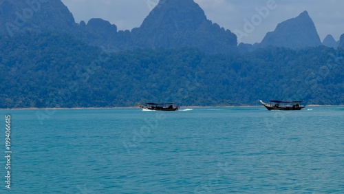 Tableau sur toile Traditional boats sailing by the cinematic limestone cliffs of Cheow Lan Lake, Khao Sok