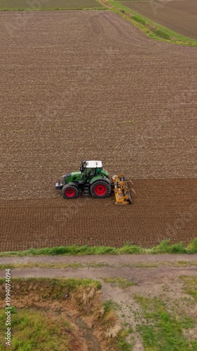 Tractor Plowing Field: An agricultural tractor diligently plows a vast brown field under an overcast sky, preparing the soil for the next planting season, showcasing the essence of rural industry.