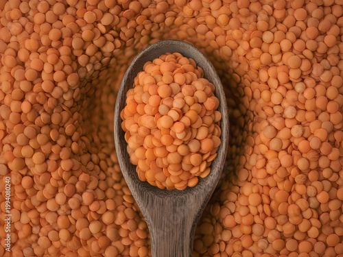 Wooden spoon filled with red lentils on a bed of scattered lentils