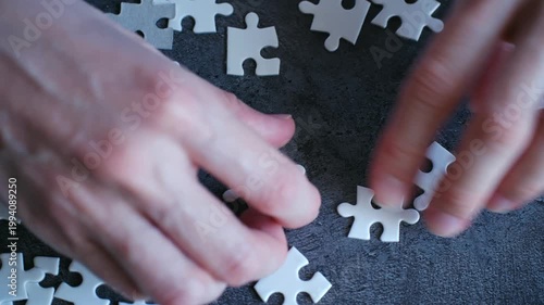 Close up hands assembling blank white jigsaw puzzle, symbolizing problem solving, strategy, teamwork. Business concept for finding solution, achieving success together. Hands connecting puzzle pieces.