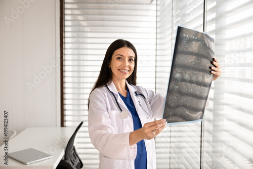Portrait of smiling female doctor examining mri film, performing x-ray analysis, reviewing radiology results in hospital office. Healthcare treatment planning, medical diagnosis and health checkup