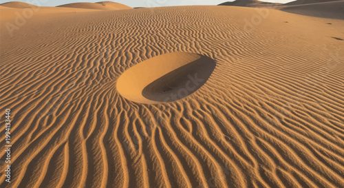 Wide angle view of orange sand dunes in a desert landscape featuring intricate wind-swept ripple patterns and a singular oval-shaped depression casting a dark shadow at sunset.