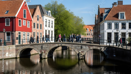 People walk across a bridge over a canal in a city with colorful buildings