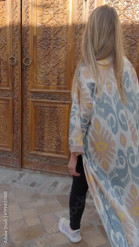 Woman in Uzbek robe opening carved wooden door in Tashkent old city