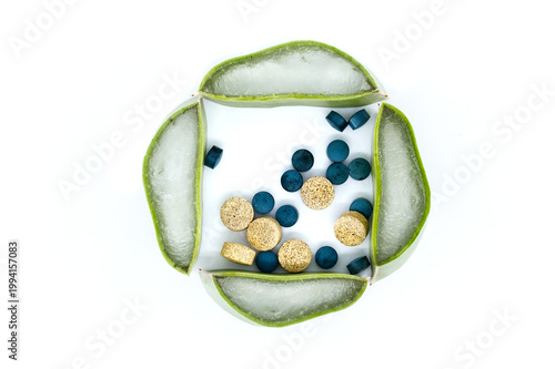 Aloe vera slices arranged with blue and tan pills on a white background