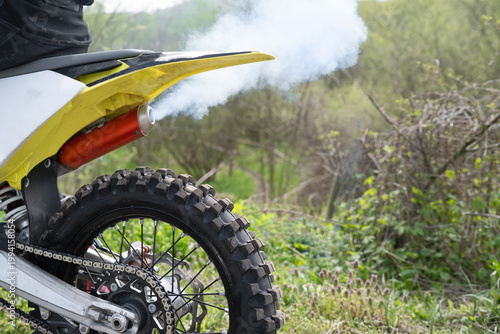 Εκτύπωση καμβά Close-up of a motorcycle exhaust pipe emitting white smoke in the woods, rear wheel of a dirt bike on a forest trail, off-road power and engine concept