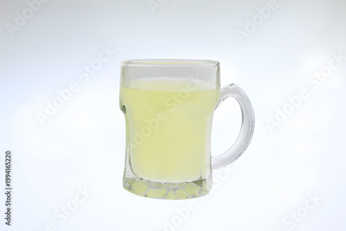 Fresh infused water in a transparent glass mug isolated on white background. Glass mug holds pale yellow liquid.  healthy detox water, vitamin C infused drink, cold refreshing natural immune booster. 