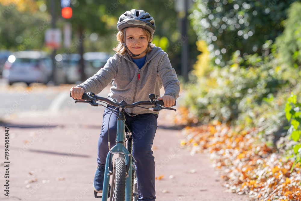 Fototapeta premium Child rides bike on autumn. Kid wearing bike helmet. Happy child learning to bike ride. Child with bicycle in autumn fall park. Fall city scene with child on bike.