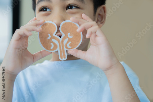 Foto Little cute Asian chid boy with paper kidneys and looking outside at home