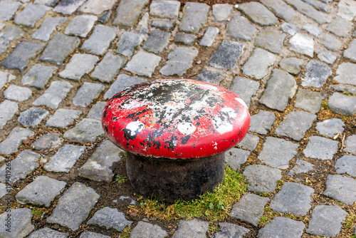 Schilderij op canvas Weathered red mooring bollard on cobblestone pavement
