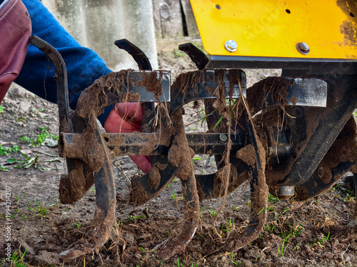 Agronomist hand removing dirty tilling blades from a walk-behind tractor, preparing farming equipment for spring soil cultivation and planting activities.