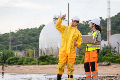 Environmental scientist in yellow hazmat suit inspecting water sample near industrial plant, Ecologists team analyzing water pollution and quality near oil refinery or gas storage