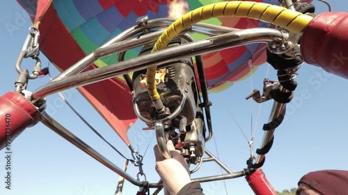 A vibrant hot air balloon with a colorful pattern is being inflated under a clear blue sky, viewed from the basket.