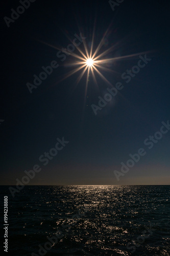Sun star flare over dark sea horizon at night