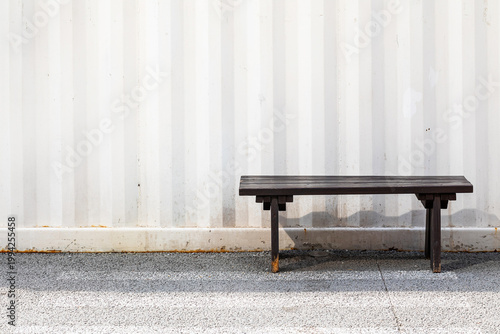 Dark wooden bench in front of white corrugated metal wall